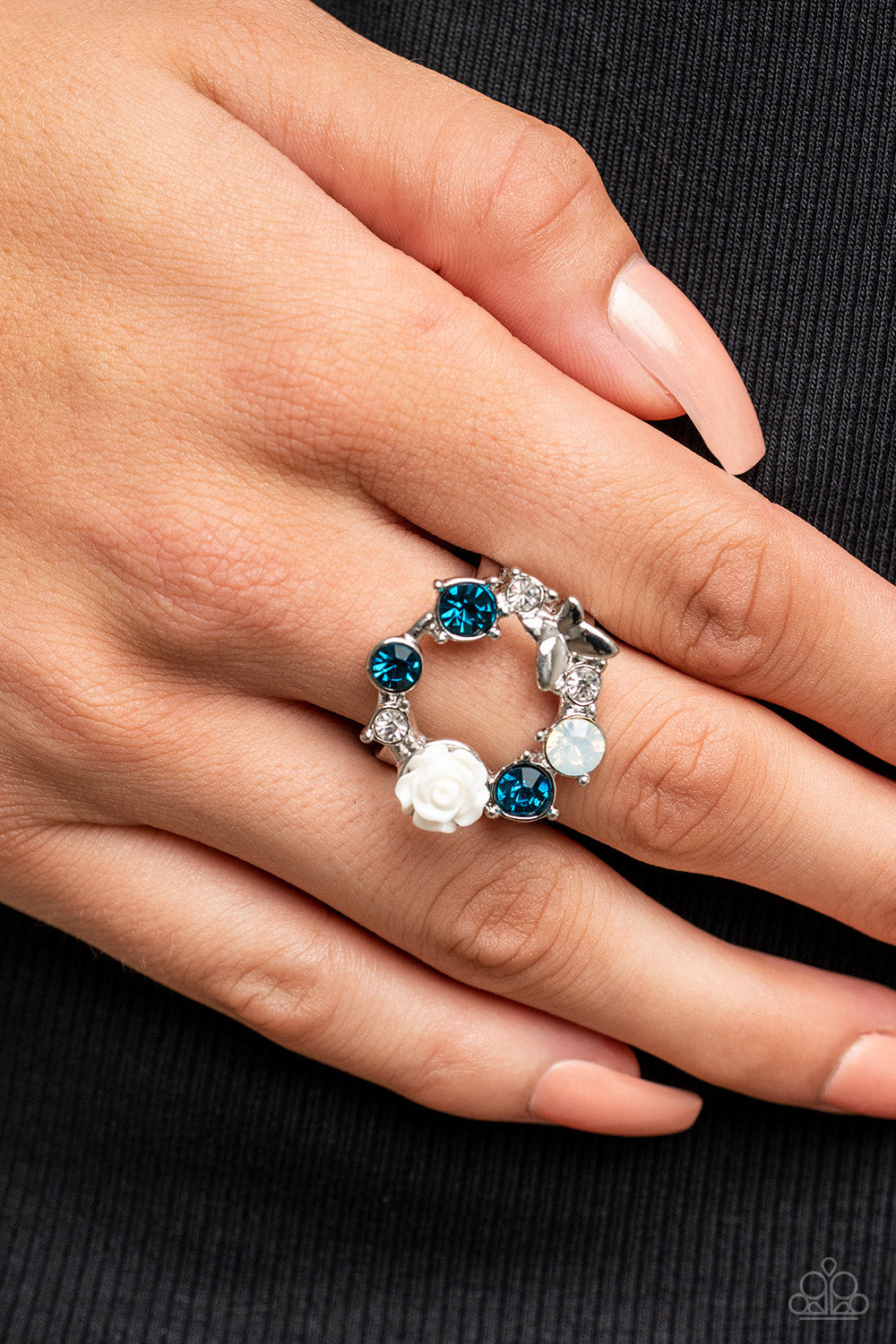 Butterfly Bustle - Blue and Silver Ring - Paparazzi Accessories - A glitzy collection of blue, opal, and white rhinestones coalesce into a sparkly wreath atop the finger. Elegantly enhanced with a white resin rosebud, a dainty silver butterfly flutters atop the glittery centerpiece for an enchanting finish. Features a stretchy band for a flexible fit. Sold as one individual ring.