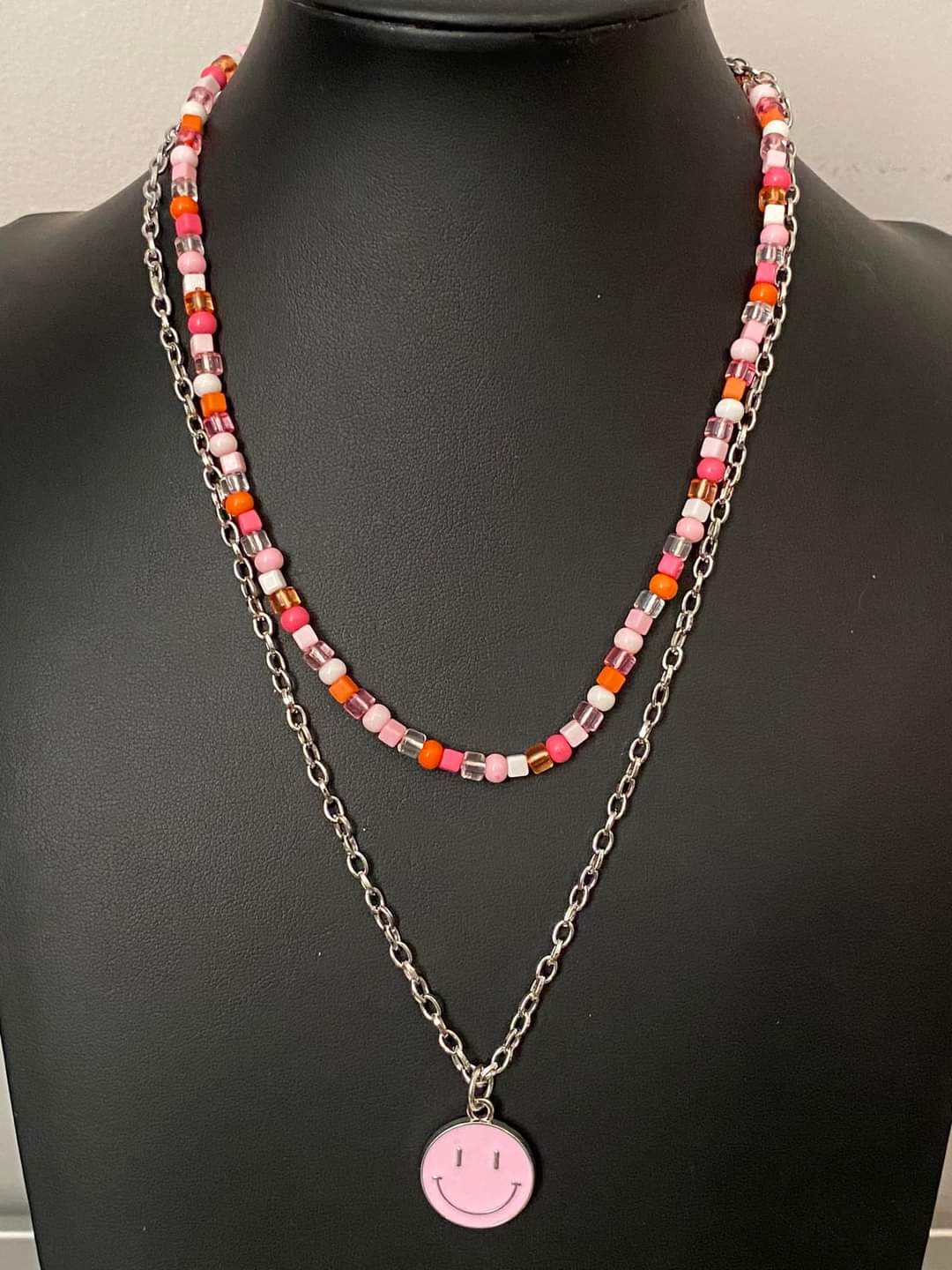 High School Reunion - Pink Seed Bead Necklace - Paparazzi Accessories - Gliding from a dainty, silver chain, a smiley face pendant stands out against a pink backdrop. Completing the charismatic ensemble, a collection of seed beads in shades of light pink, white, pink, orange, and hot pink create bright pops of color around the neckline for a youthful finish.