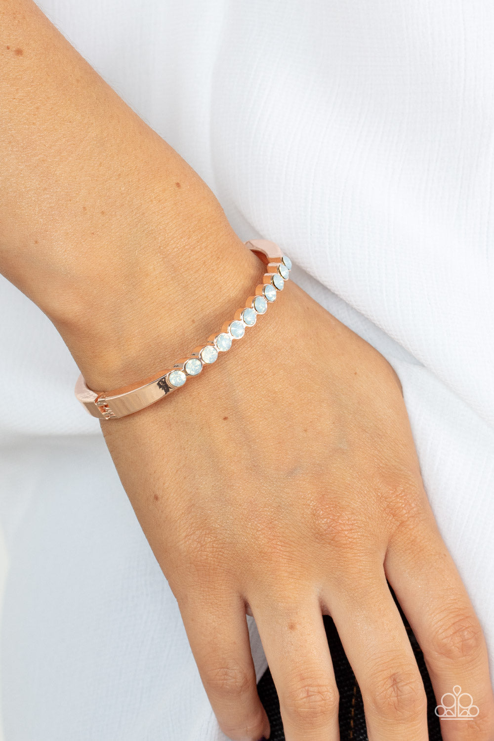 Mystical Masterpiece - Rose Gold Hinge Bracelet - Paparazzi Accessories - An opalescent row of white rhinestones hinges to a glistening rose gold bar that curves around the wrist, creating a sparkly cuff-like bracelet. Features a hinged closure.