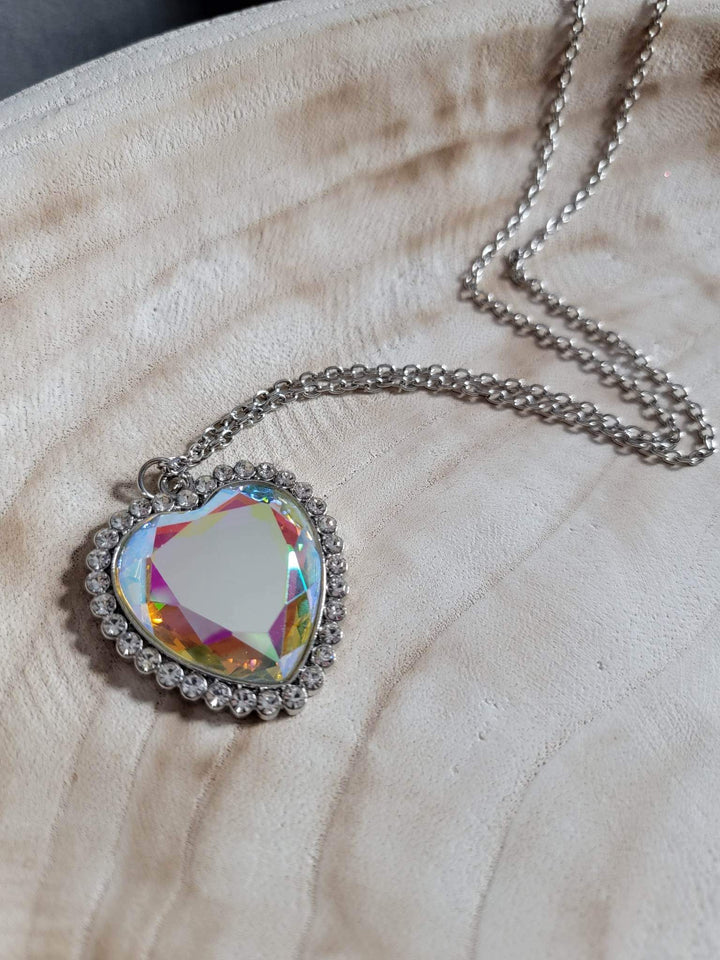 Prismatically Twitterpated - Multi Color Heart Necklace - Paparazzi Accessories - Bordered in glassy white rhinestones, an oversized iridescent heart gem sparkles from the bottom of an extended silver chain for a flirty finish. Features an adjustable clasp closure. Due to its prismatic palette, color may vary. Sold as one individual necklace.