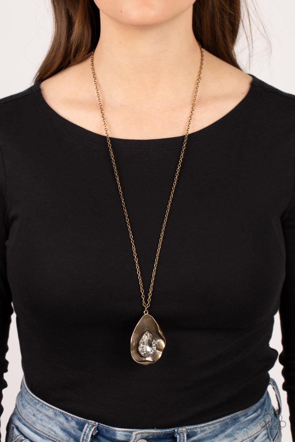 Surrealist Sparkle - Brass Necklace - Paparazzi Accessories - A warped brass frame gently folds around an oversized white teardrop gem center, resulting in a gritty yet glamorous pendant at the bottom of a lengthened brass chain.
