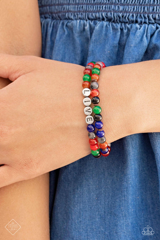 BEAD That As It May - Multi Color Bracelet - Paparazzi Accessories - Countless stone beads in a range of vibrant colors are threaded along a pair of stretchy bands to create a stack of earthy bracelets. Silver discs stamped with black letters are centered within one of the colorful strands, spelling out the word, "LIVE," in an inspirational finish. Sold as one set of two bracelets.