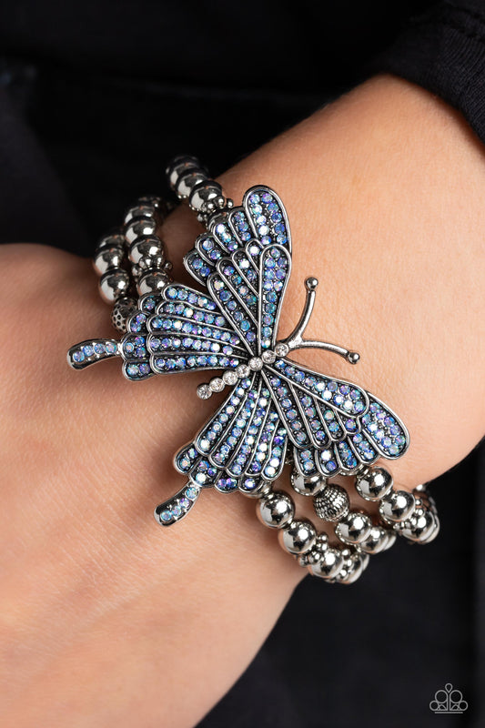 First WINGS First - Blue and Silver Butterfly Bracelet - Paparazzi Accessories - Strung along elastic stretchy bands, a trio of silver and textured silver beads and accents wrap around the wrist. Featured atop the beaded collection, an oversized silver butterfly, with intricate details, is sprinkled with dainty blue iridescent rhinestones across its wings and body, for a dramatically dazzling finish.