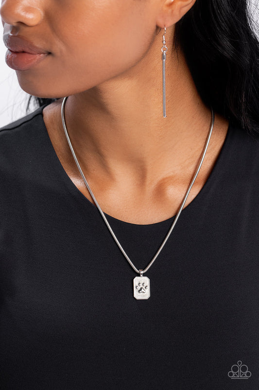 PAW to the Line - Silver Necklace - Paparazzi Accessories - Dangling from a sleek silver snake chain, a rectangular pendant glides down the chest. Featured within the pendant, a silver pawprint, surrounded by white pearl paint creates an elegant pet-inspired pendant.