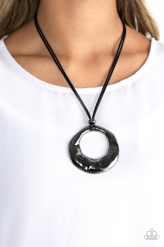 Tectonic Treasure - Black Gunmetal Necklace - Paparazzi Accessories - An oversized, oblong, gunmetal hoop rippling with hammered textures swings from the bottom of a collection of black cording. A single gunmetal bead glides down the bottom of the cording for a dramatic industrial look, anchoring the cording to the hoop.