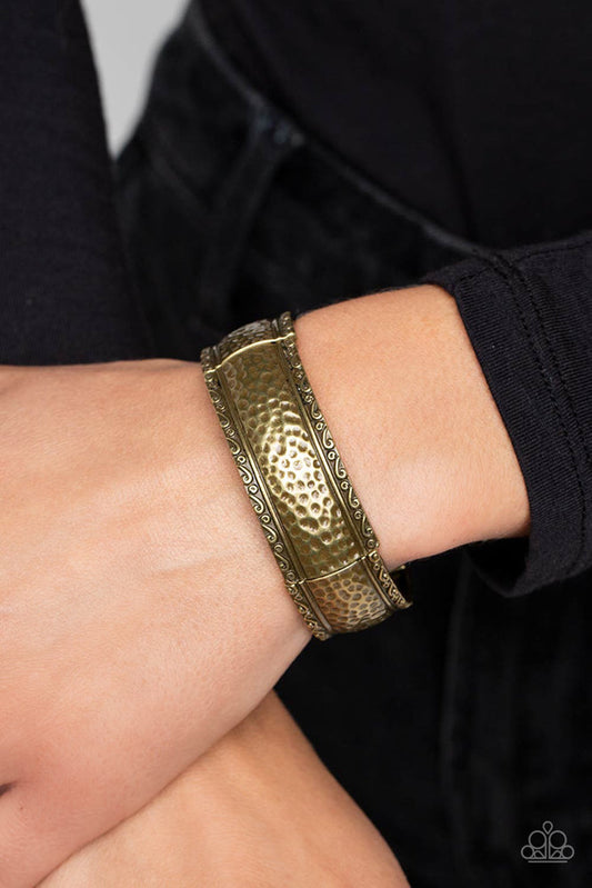 Textile Tenor - Brass Bracelet - Paparazzi Accessories - Curved frames of antiqued brass curve around the wrist on elastic stretchy bands. Studs and ribbons of brass curl into a dainty filigree above and below its hammered center for a soft and dauntless combo.