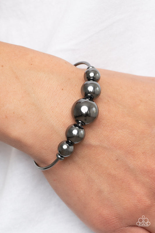 Bead Creed - Black Gunmetal Bracelet - Paparazzi Accessories - Gradually increasing in size, an oversized collection of gunmetal beads are threaded along a dainty gunmetal cuff for a dramatic industrial display. Sold as one individual bracelet.