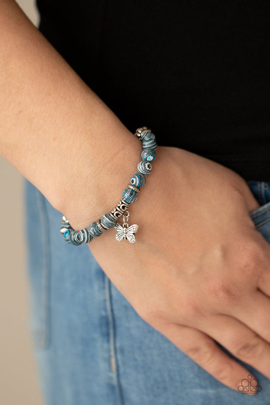 Butterfly Wishes - Blue and Silver Bracelet - Paparazzi Accessories - Swirling with blue, black, and white accents, colorful stone beads and ornate silver accents are threaded along stretchy bands around the wrist. A dainty silver butterfly charm dangles from the display, adding a whimsical flair.