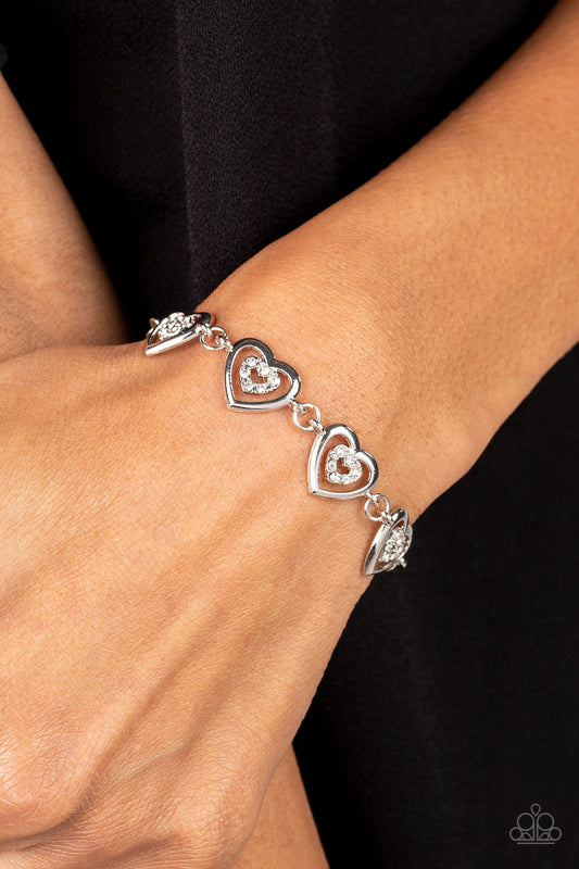 Catching Feelings - White and Silver Heart Bracelet - Paparazzi Accessories - Dotted with dainty white rhinestones, airy silver heart silhouettes are affixed to the points of larger silver heart frames. The two dimensional heart frames link together around the wrist in a flirtatious finish. Features an adjustable clasp closure. Sold as one individual bracelet.