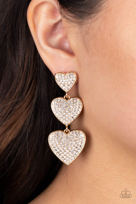 Couples Retreat - Gold Heart Earrings - Paparazzi Accessories - Three white rhinestone-studded gold hearts gradually increase in size as they cascade down the ear in a shimmery display. Each of the hearts interconnect to one another adding a shifting, whimsical detail to the spritz of glitz. Earring attaches to a standard post fitting. Sold as one pair of post earrings.