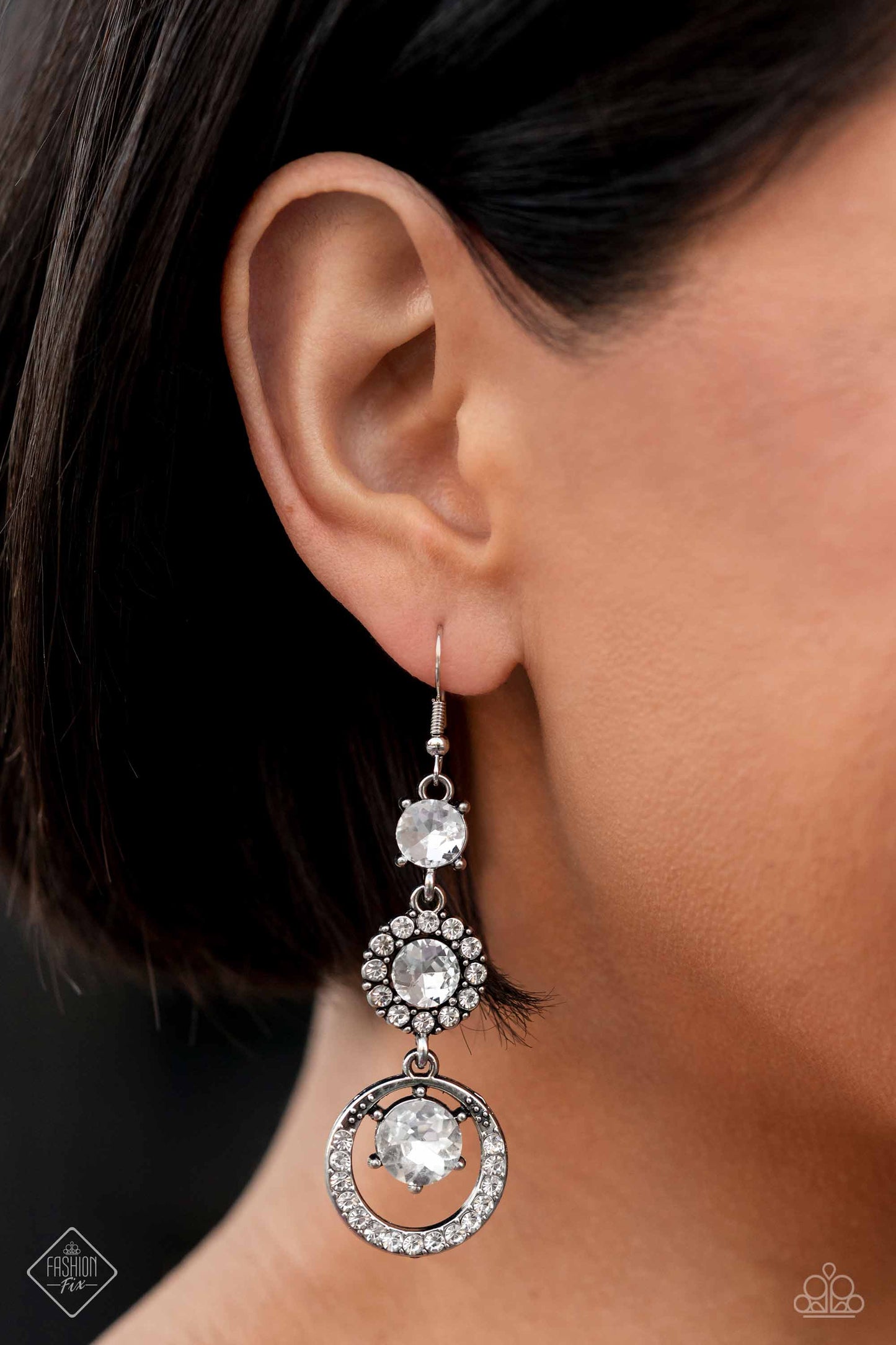 Enchanting Effulgence - White Gem and Silver Earrings - Paparazzi Accessories - A glamorous collection of brilliant, round, white gems drip down the ear, creating an irresistibly refined lure. The topmost gem features pronged fittings, followed by the center gem that is bordered by a halo of dainty white rhinestones for additional eye-catching shimmer. Encircling the lower-most gem, an airy, rhinestone-encrusted hoop completes the dazzling design.