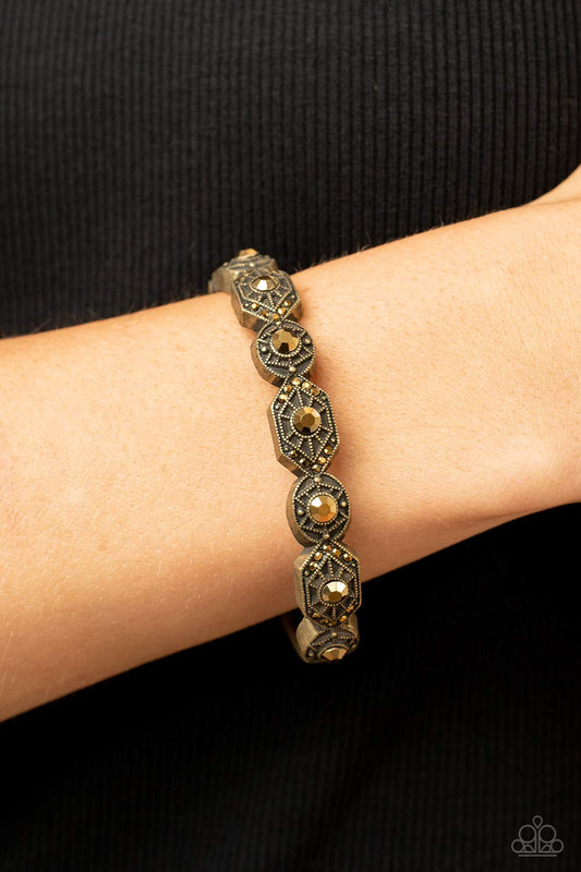 Eye-Opening Opulence - Brass Bracelet - Paparazzi Accessories - Dotted with dainty aurum rhinestones, geometrically patterned brass frames alternate across the front of a bangle-like bracelet for an edgy pop of shimmer. Features a hinged closure. Sold as one individual bracelet.