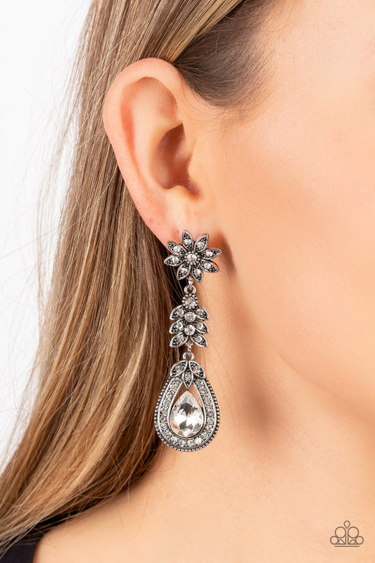 Floral Fantasy - Silver and White Earrings - Paparazzi Accessories - Dotted in dainty white rhinestones, a studded silver flower gives way to a leafy frame that is delicately suspended above a decorative white rhinestone dotted teardrop frame. An oversized teardrop gem seemingly floats inside the center of the lowermost frame, adding timeless dazzle to the floral fairytale. Earring attaches to a standard post fitting. Sold as one pair of post earrings.