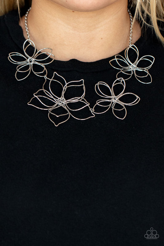 Flower Garden Fashionista - Large Blossoms - Silver Flower Necklace - Paparazzi Accessories - Shiny silver wire delicately twists into oversized blossoms. Varying in size, the airy floral frames delicately link into an asymmetrical display as the layered frames elegantly pop beneath the collar. Features an adjustable clasp closure. Sold as one individual necklace.