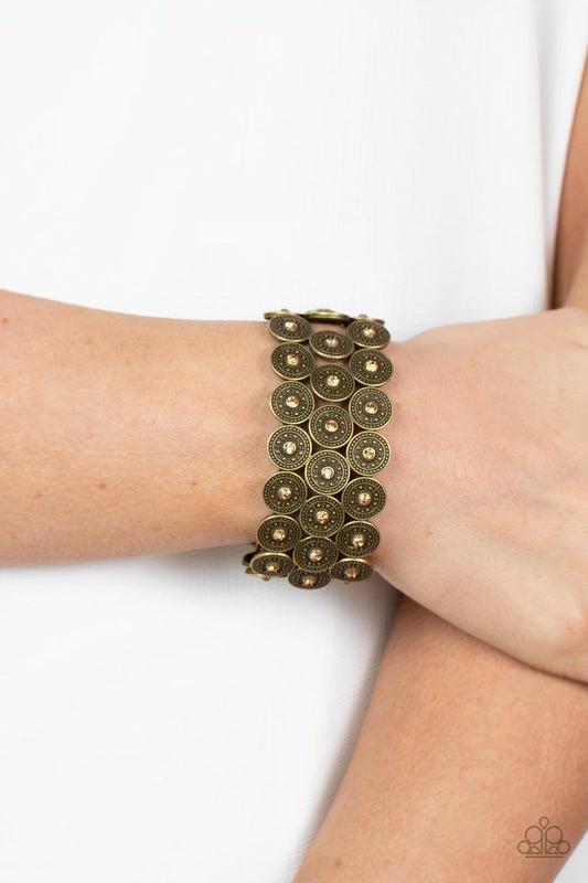 Forgotten Treasure - Brass Bracelet - Paparazzi Accessories - Dotted with dainty golden topaz rhinestone centers, studded brass discs haphazardly stack into trios that have been threaded along stretchy bands around the wrist for a whimsical finish.
