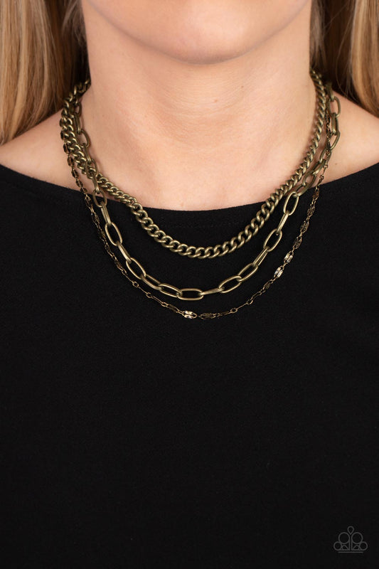 Galvanized Grit - Brass Necklace - Paparazzi Accessories - Three different kinds of weighted brass chains layer down the neck to create a gritty, edgy statement piece. Features an adjustable clasp. Sold as one individual necklace.