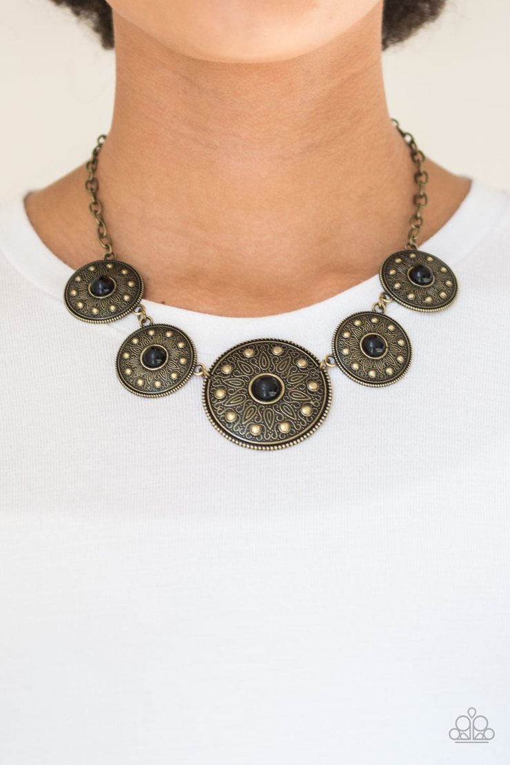 Hey, SOL Sister - Black and Brass Necklace - Paparazzi Accessories - Gradually increasing in size near the center, round brass frames radiating with sunburst patterns link below the collar. Infused with shiny brass studs, the tribal inspired frames are dotted with black beaded centers for a colorful finish. Features an adjustable clasp closure. Sold as one individual necklace.