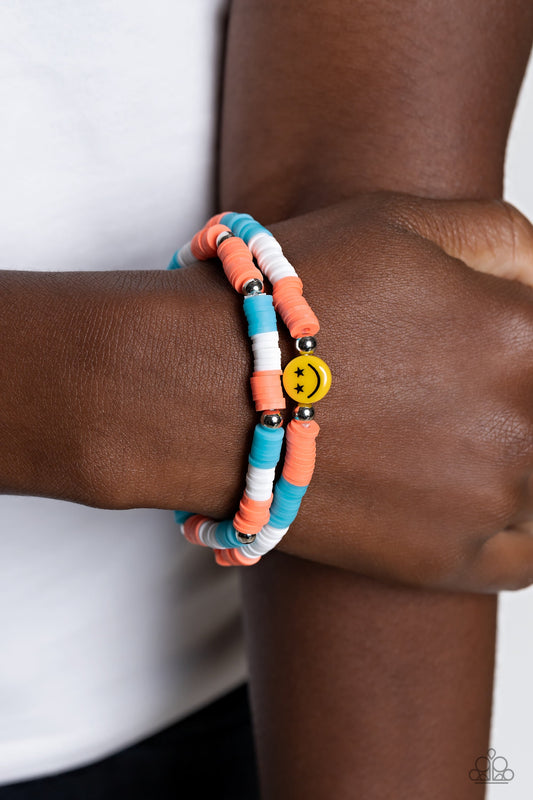 In SMILE - Orange and Blue Bracelet - Paparazzi Accessories - Coral, blue, and white rubber discs combine with sporadically placed silver beads to provide a vibrant pop of color along the wrist. Meeting in the center of one of the multi-shaded bracelets, a yellow bead with a smiley face, featuring stars for eyes.