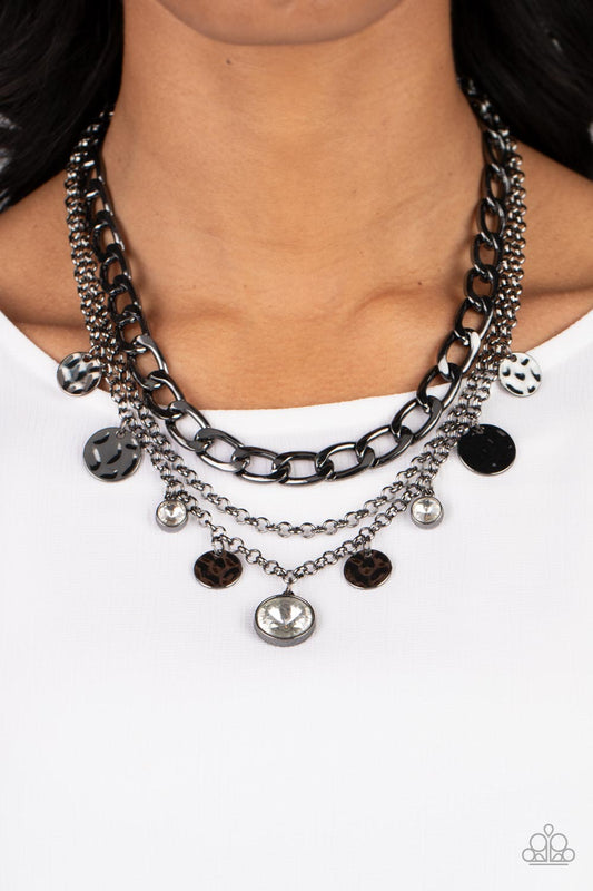 Industrial Noise - Gunmetal - Black Metal Necklace - Paparazzi Accessories - A thick strand of gunmetal curb chain drapes across the chest between two gunmetal bars, forming the first of three layers. A classic gunmetal chain falls below, for a simple reprieve before  the final strand of gunmetal chain below. Hammered gunmetal discs and brilliant white gems encased in gritty gunmetal fittings dance along the bottom chain, adding a hint of glitzy to the industrial design.