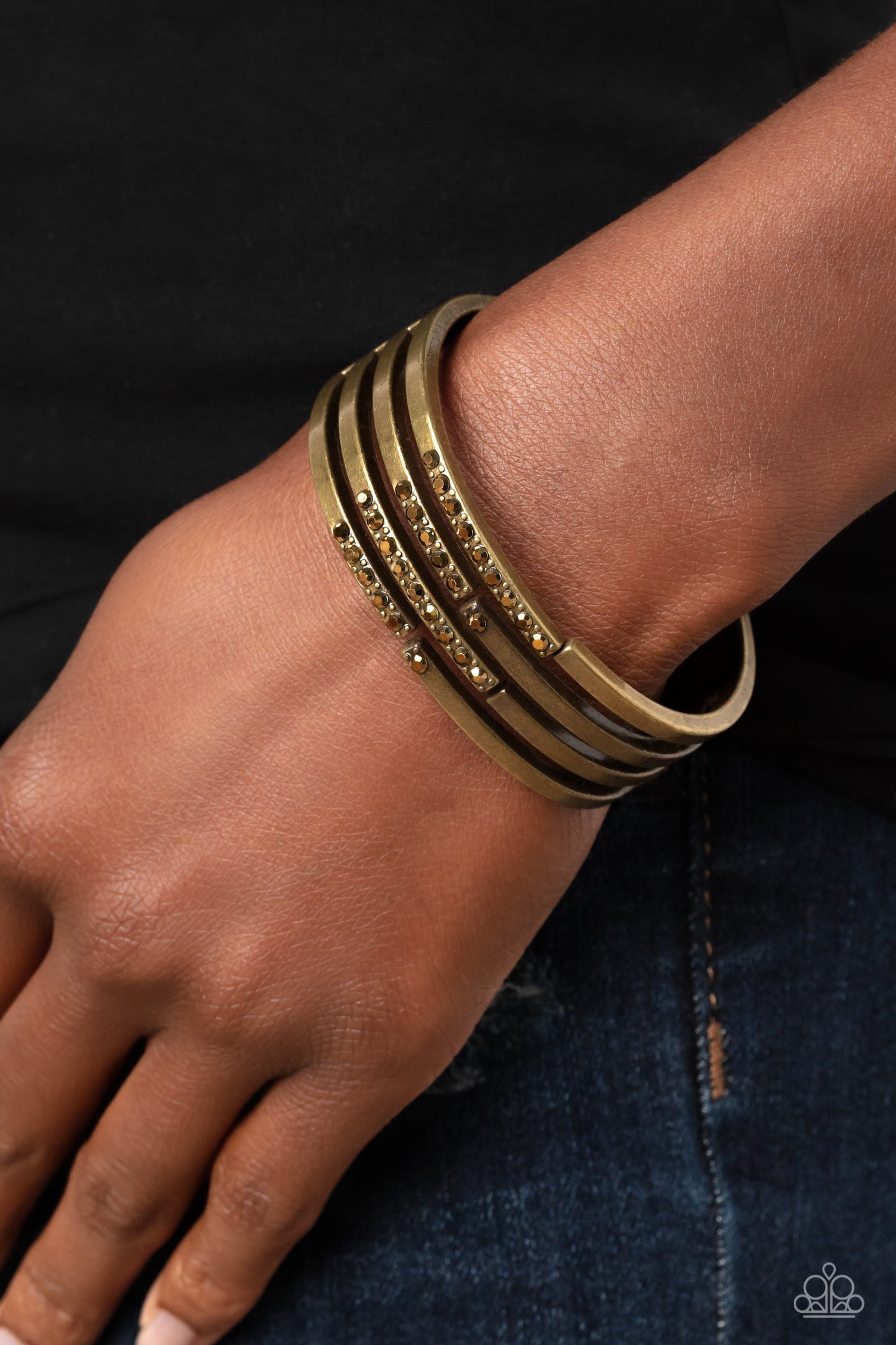 Labyrinth Lure - Brass Bracelet - Paparazzi Accessories - Linear layers of brass stream from a solid piece of brass for an industrial vibe. Featured on the various streams of brass bars, aurum gems and studs coalesce across the surface for a subtle pop of shimmer atop the wrist. The skin peeks out from the scattered bars for additional eye-catching detail. Features a hinged closure.