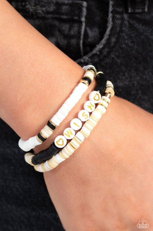 Matriarchal Melody - Black And Gold Wish Bracelet - Paparazzi Accessories - Varying in shades, tan, black, and white clay discs pair with shiny gold disc beads and accents creating layers across the wrist. Featured on one of the bracelets, white beads stamped with gold lettering spell out the word "wish," while gold heart silhouettes stamped in the same white beads frame the inspirational phrase for a wistful finish.