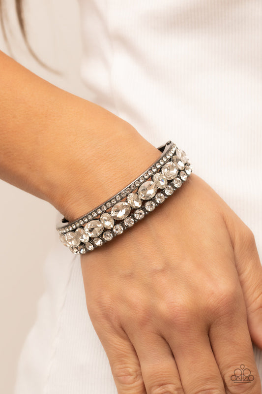 Mega Megawatt - Black Gunmetal Bracelet - Paparazzi Accessories - Three blinding rows of mismatched white rhinestones dramatically stack across the wrist, coalescing into a majestic bangle-like centerpiece. Features a hinged closure. Sold as one individual bracelet.