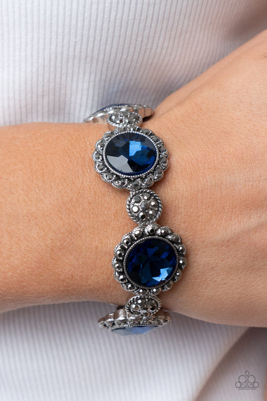 Palace Property - Blue and Silver Bracelet - Paparazzi Accessories - An oversized blue rhinestone adorns the center of a hematite rhinestone petaled floral frame. Infused with hematite dotted silver accents, the glitzy floral frames sparkle along stretchy bands around the wrist for a glamorous finish. Sold as one individual bracelet.