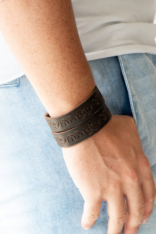Ride and Wrangle - Urban Brown Snap Bracelet - Paparazzi Accessories - Split down the center, a distressed brown leather band has been stamped in a traditional western pattern for a rustic look. Features an adjustable snap closure. Sold as one individual bracelet.