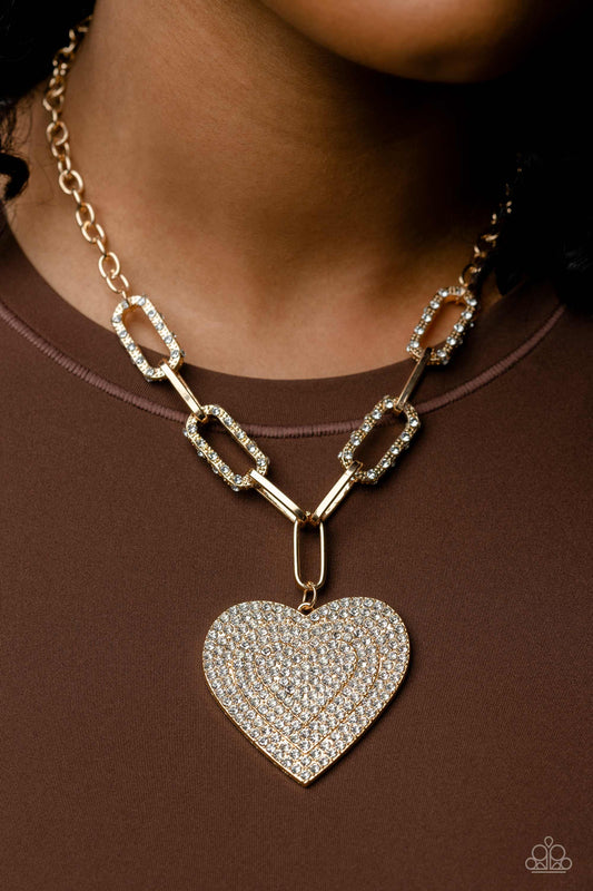 Roadside Romance - Gold Heart Necklace - Paparazzi Accessories - Elongated, oversized gold links, encrusted with a blinding display of white rhinestones and shimmery gold accents connect a classic gold chain to an exaggerated gold heart pendant for a romantically refined finish. Featured on the oversized gold heart, layers upon layers of glitzy white rhinestones emboss across its entire surface as the hearts gradually increase in size from the center.