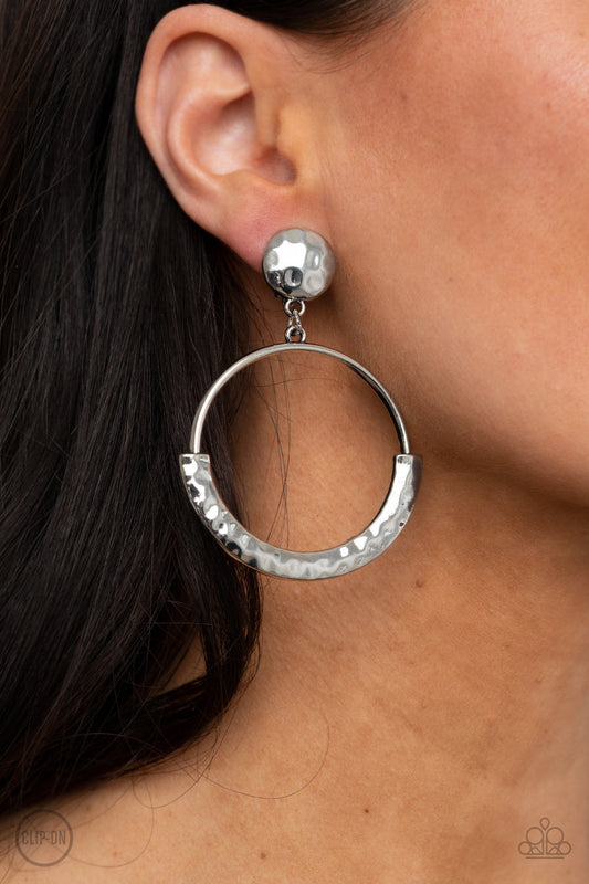 Rustic Horizons - Silver Clip-On Earrings - Paparazzi Accessories - The bottom of an antiqued silver hoop is covered with a bowing hammered frame at the bottom of a hammered silver disc, creating a rustic lure. Earring attaches to a standard clip-on fitting. Sold as one pair of clip-on earrings.