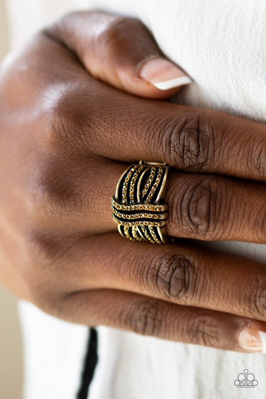 Showbiz Beauty - Brass - Topaz Ring - Flexible Fit Band - Paparazzi Accessories - Encrusted in glittery topaz rhinestones, glistening brass bands wave across the finger, stacking into a refined band. Features a stretchy band for a flexible fit. Sold as one individual ring.