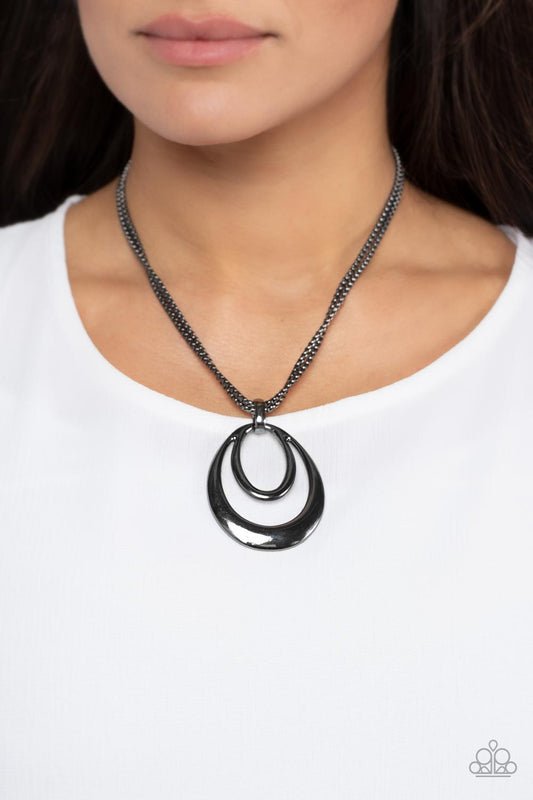 Suburban Storm - Black Gunmetal Necklace - Paparazzi Accessories - Two shiny gunmetal oval frames delicately coalesce into a glistening pendant at the bottom of layered rows of gunmetal box chain, creating a classic metallic look below the collar. Features an adjustable clasp closure. Sold as one individual necklace.