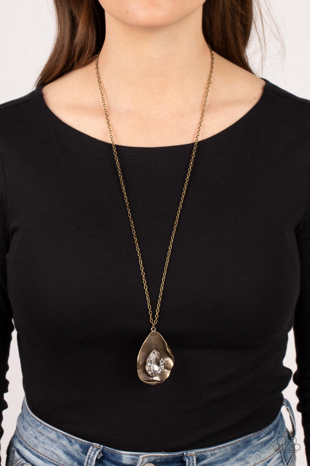 Surrealist Sparkle - Brass Necklace  - Paparazzi Accessories - A warped brass frame gently folds around an oversized white teardrop gem center, resulting in a gritty yet glamorous pendant at the bottom of a lengthened brass chain. 
