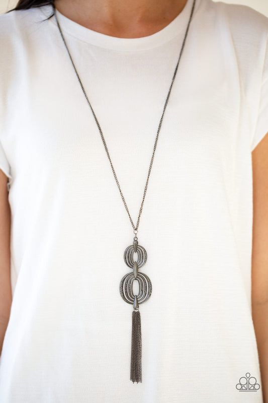 Timelessly Tasseled - Black Necklace - Paparazzi Accessories - Delicately hammered in sections of shimmer, gunmetal circular frames stack into a bold pendant at the bottom of a lengthened gunmetal chain. A shimmery gunmetal tassel swings from the bottom of the stacked pendant for a casual finish.