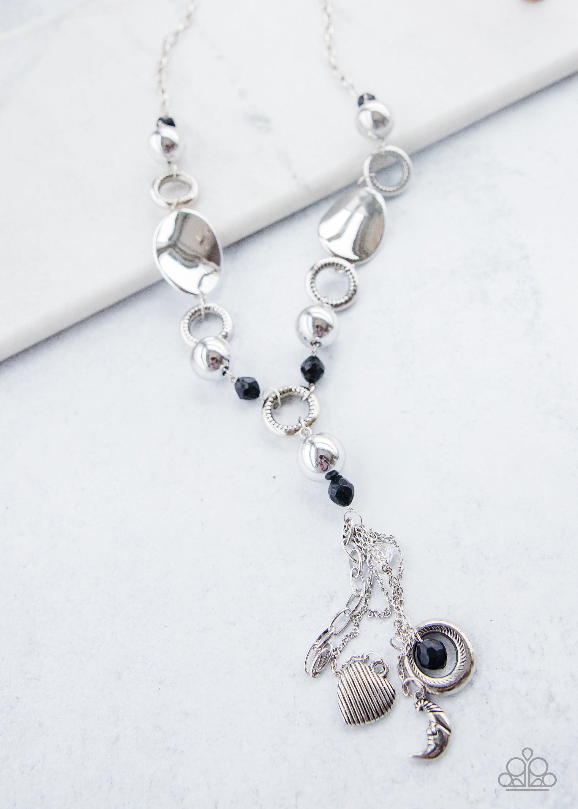 Total Eclipse Of the Heart - Silver and Black Necklace - Paparazzi Accessories -  Bejeweled By Kristie - Long chain of black crystalized beads, curved plates of silver with a pearly finish, and chunky silver rings lead down to a tassel of chains and charms, including a crescent moon and a heart. 