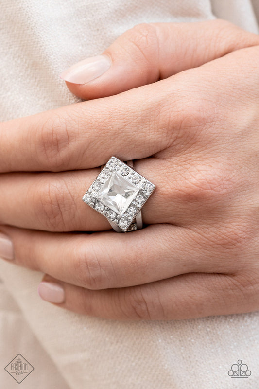 Transformational Twinkle - White and Silver Fashion Ring - Paparazzi Accessories - An oversized, square-cut, white rhinestone is tilted on a point and framed by tiny white gems. As it sits atop a pair of sleek silver bands, the faceted surface of the centerpiece catches and reflects the light of the accents that surround it, magnifying its impressive impact. Features a dainty stretchy band for a flexible fit. Sold as one individual ring.