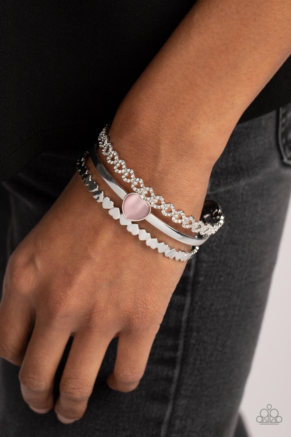 You Win My Heart - Pink and Silver Heart Bracelet - Paparazzi Accessories - Three bands of silver arc across the wrist to create a romantic-inspired cuff. A row of white rhinestone-studded hearts are turned on their sides, gracing the top band of the cuff while solid silver hearts alternate end-over-end to create the bottom band. A sleek bar of silver topped with a light pink, heart-shaped, cat's eye stone falls between the outer bands, emerging as a polished focal point in a whimsical finish.